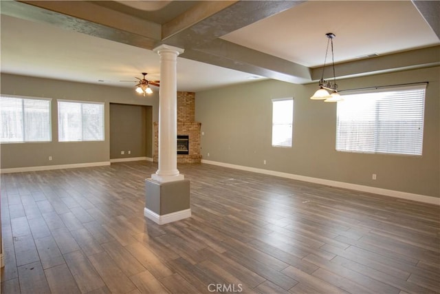 unfurnished living room featuring a ceiling fan, dark wood-style floors, baseboards, and ornate columns