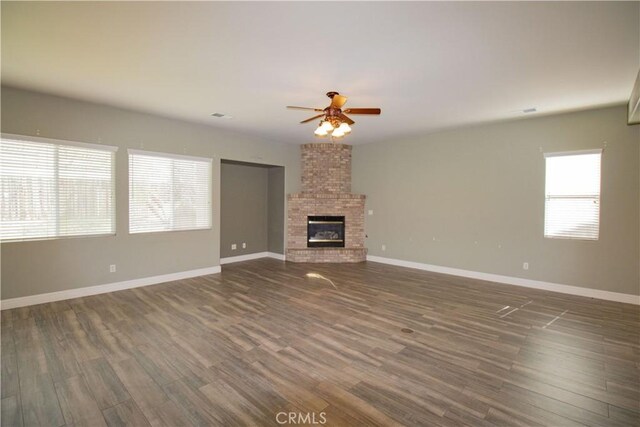 unfurnished living room featuring baseboards, dark wood-type flooring, a brick fireplace, and a ceiling fan