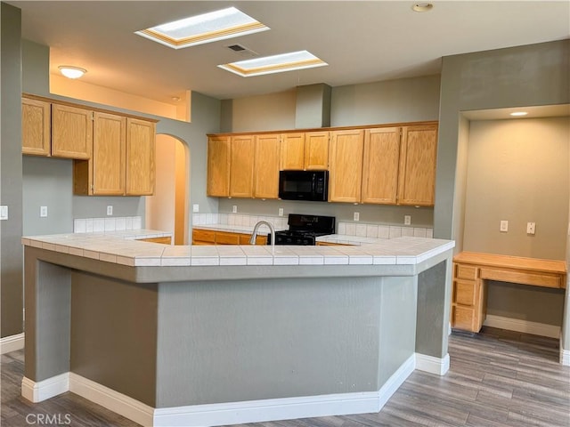 kitchen featuring a sink, arched walkways, black appliances, and wood finished floors