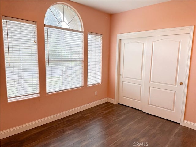 unfurnished bedroom with a closet, baseboards, and dark wood-style floors