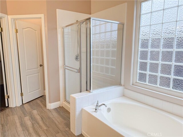 full bathroom featuring a shower stall, a garden tub, and wood finished floors