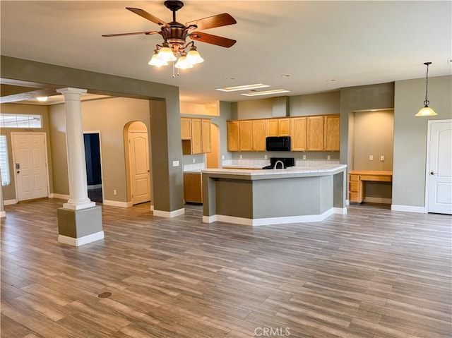 kitchen with ornate columns, light countertops, wood finished floors, and black microwave