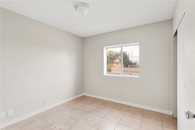 empty room with light tile patterned floors, a textured ceiling, and baseboards