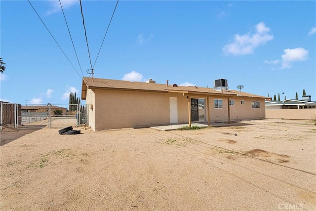 back of property featuring a gate, stucco siding, central AC, and fence