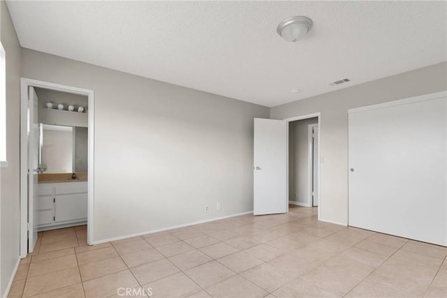 unfurnished bedroom with light tile patterned floors, baseboards, visible vents, ensuite bath, and a textured ceiling