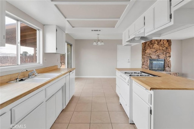 kitchen featuring a sink, a stone fireplace, white cabinets, light tile patterned floors, and white range with gas stovetop