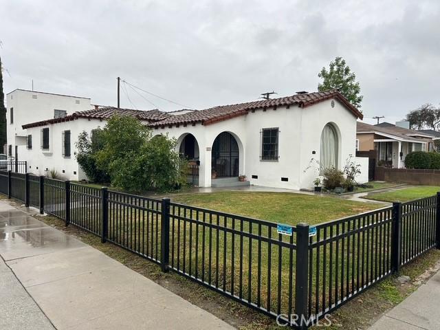 mediterranean / spanish-style house featuring a front lawn, a tiled roof, a fenced front yard, and stucco siding