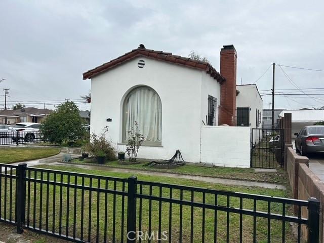 exterior space featuring fence, a chimney, stucco siding, a tile roof, and a lawn