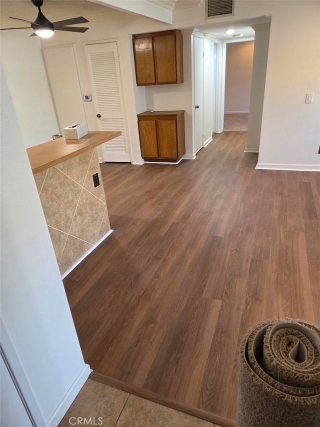 interior space with ceiling fan, baseboards, dark wood-style floors, and brown cabinetry