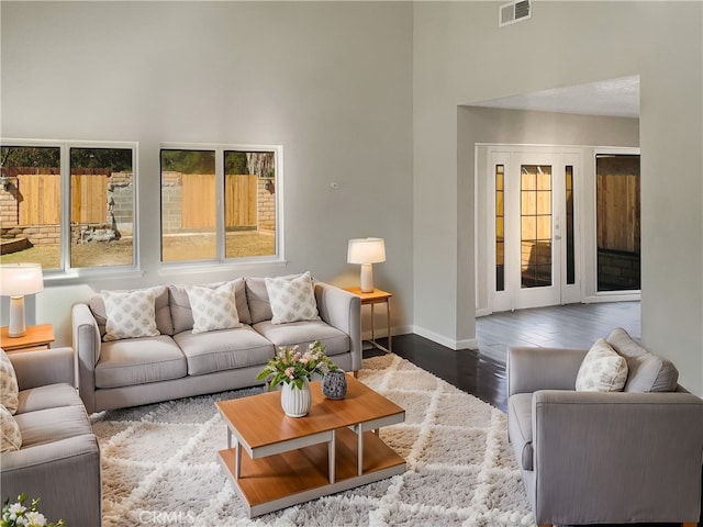 living area with wood finished floors, visible vents, a towering ceiling, and baseboards