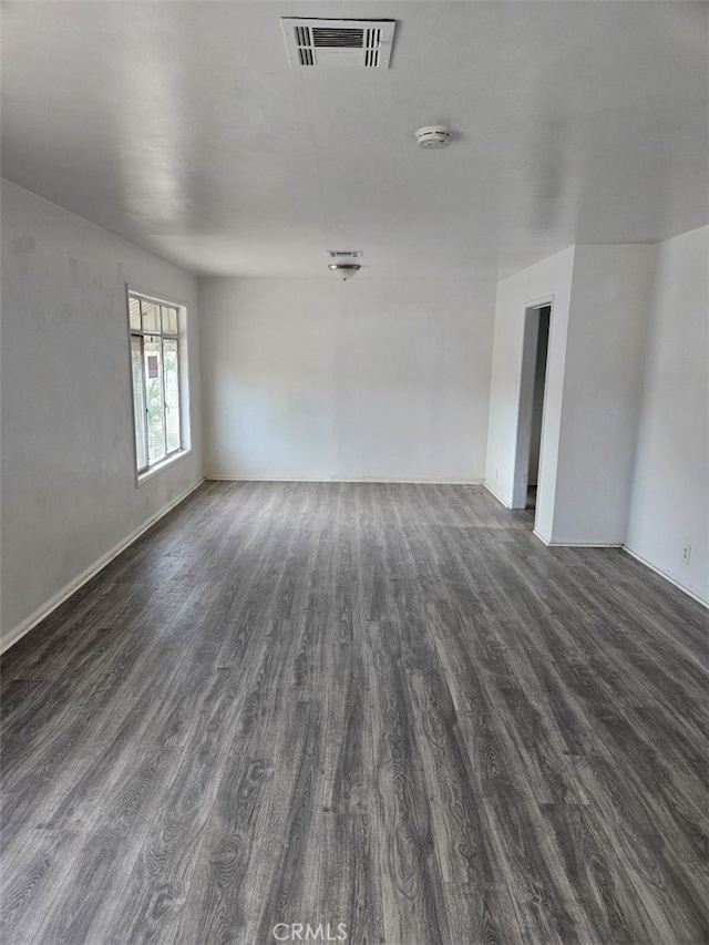 empty room with baseboards, visible vents, and dark wood-type flooring