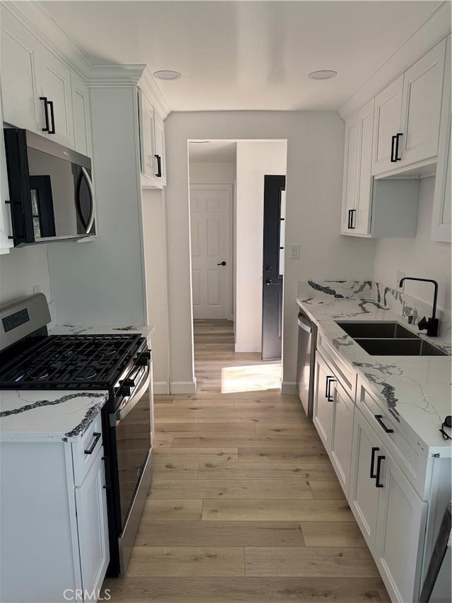 kitchen with light stone counters, a sink, stainless steel appliances, white cabinetry, and light wood-type flooring