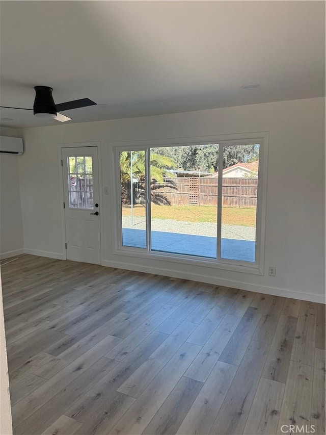 interior space with an AC wall unit, wood finished floors, baseboards, and ceiling fan