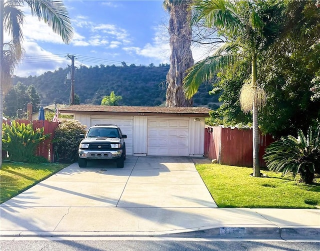 view of front of home featuring a front yard, fence, an attached garage, concrete driveway, and an outdoor structure