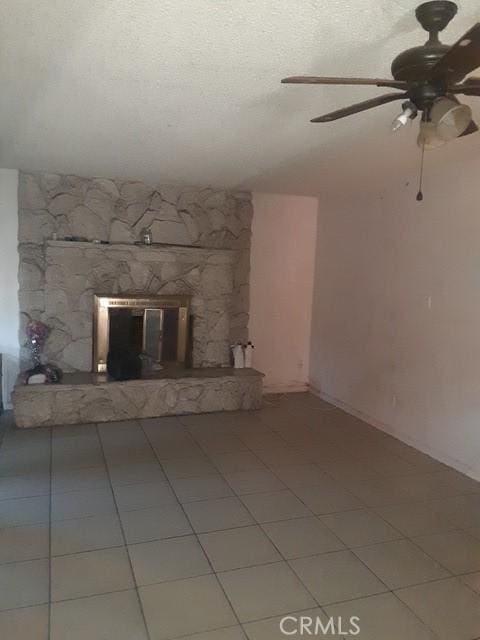 unfurnished living room with light tile patterned floors, a stone fireplace, a textured ceiling, and ceiling fan