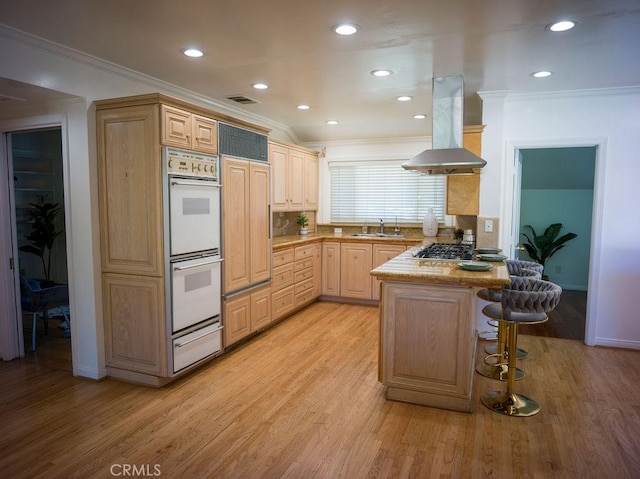 kitchen featuring light brown cabinets, island exhaust hood, a kitchen bar, double oven, and a warming drawer