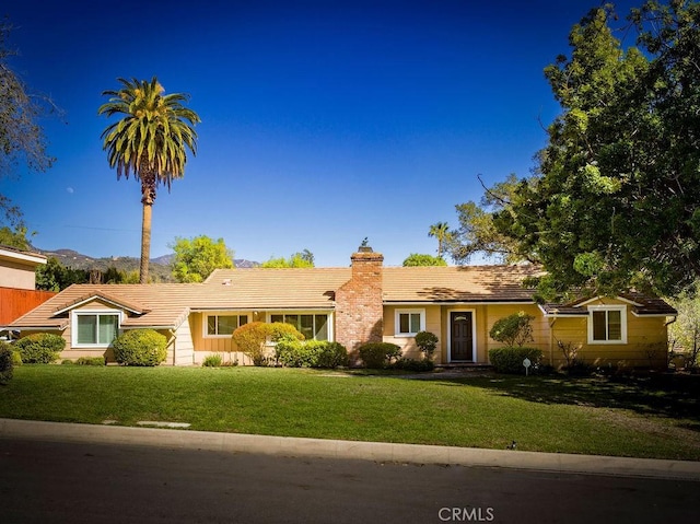 ranch-style house featuring a tiled roof, a chimney, and a front yard