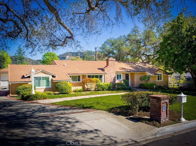 ranch-style home with a chimney, a front yard, and a tile roof