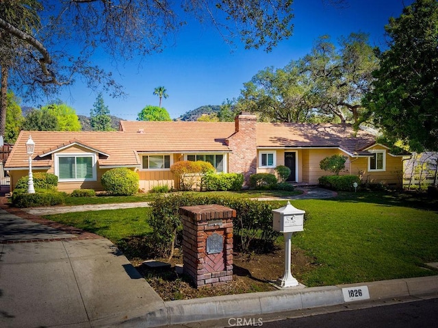 ranch-style house with a chimney, a front lawn, and a tile roof