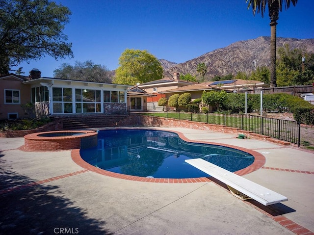 view of swimming pool with a pool with connected hot tub, fence, a patio area, a mountain view, and a diving board