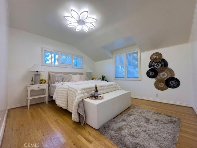 bedroom featuring baseboards, light wood-style floors, and vaulted ceiling