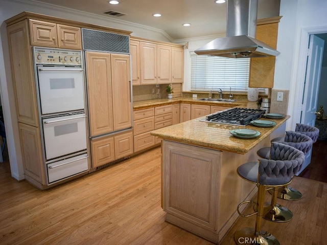 kitchen with double oven, a kitchen bar, a peninsula, island exhaust hood, and a sink