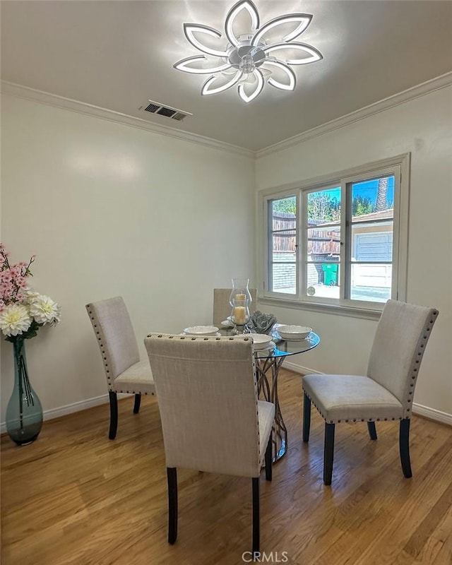 dining area with light wood finished floors, visible vents, baseboards, and ornamental molding