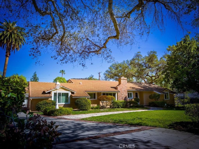 ranch-style house featuring a front yard, concrete driveway, a chimney, and a tile roof