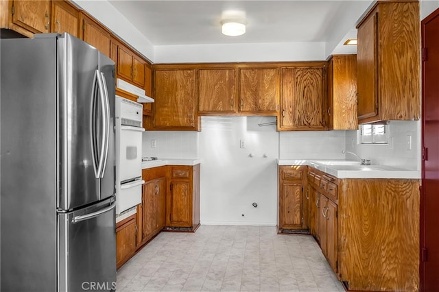 kitchen featuring oven, light countertops, brown cabinets, freestanding refrigerator, and a warming drawer