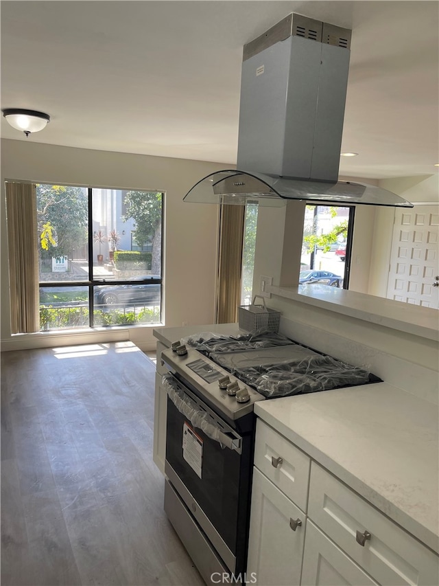 kitchen featuring island exhaust hood, stainless steel range with gas stovetop, light countertops, white cabinets, and a wealth of natural light