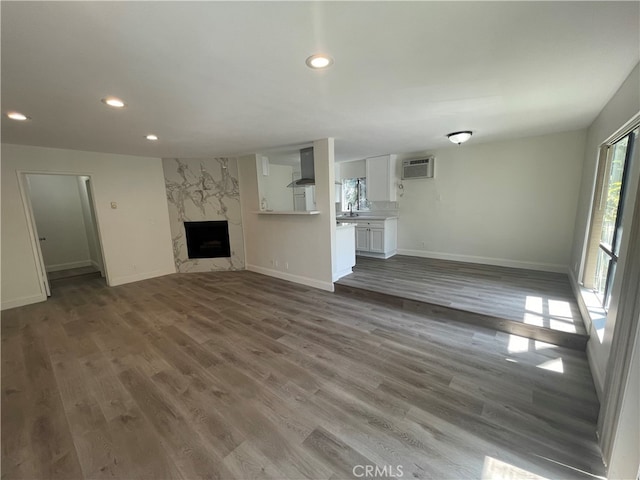 unfurnished living room with baseboards, a wall mounted AC, a premium fireplace, recessed lighting, and dark wood-style flooring