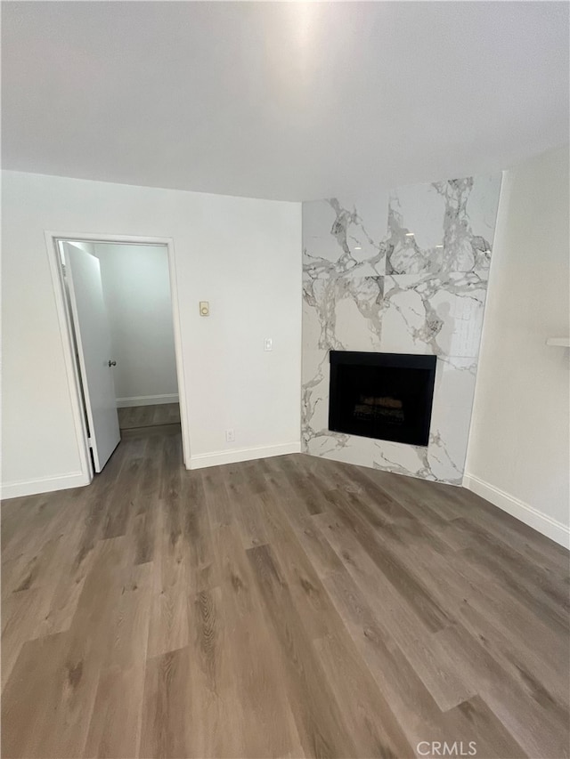 unfurnished living room featuring wood finished floors, baseboards, and a high end fireplace