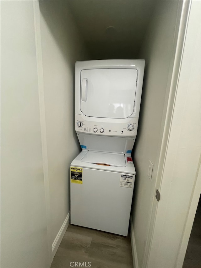 clothes washing area featuring laundry area, stacked washer / drying machine, baseboards, and wood finished floors