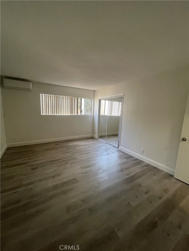 spare room featuring an AC wall unit, wood finished floors, and baseboards