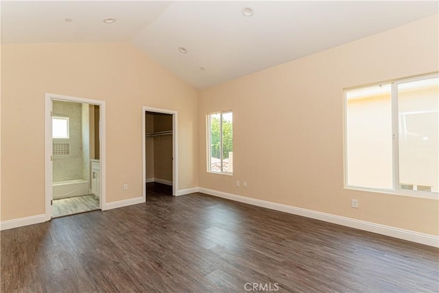 unfurnished bedroom with dark wood-style floors, baseboards, lofted ceiling, a walk in closet, and connected bathroom