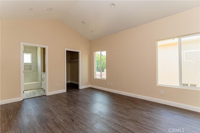 unfurnished bedroom with a spacious closet, baseboards, vaulted ceiling, dark wood-style floors, and ensuite bath