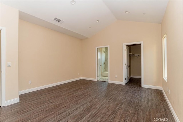 unfurnished bedroom featuring visible vents, a walk in closet, baseboards, vaulted ceiling, and dark wood-style floors