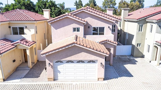 mediterranean / spanish house with stucco siding, concrete driveway, a chimney, and fence