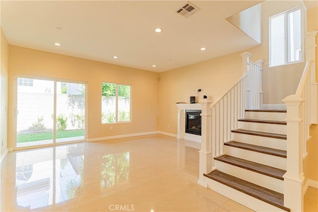 unfurnished living room with visible vents, baseboards, stairs, recessed lighting, and a glass covered fireplace