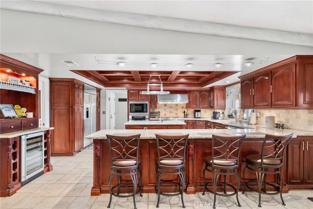 kitchen with visible vents, wall chimney range hood, black microwave, beverage cooler, and decorative backsplash