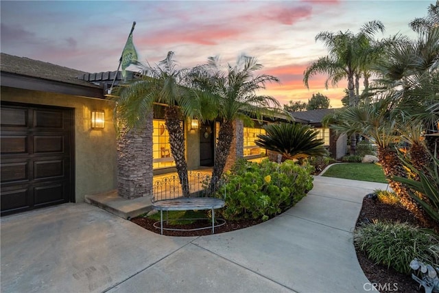 exterior entry at dusk featuring a garage, driveway, and stucco siding