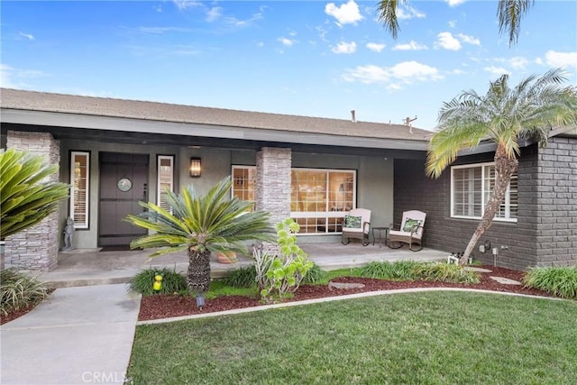 property entrance featuring brick siding, stucco siding, a porch, and a yard