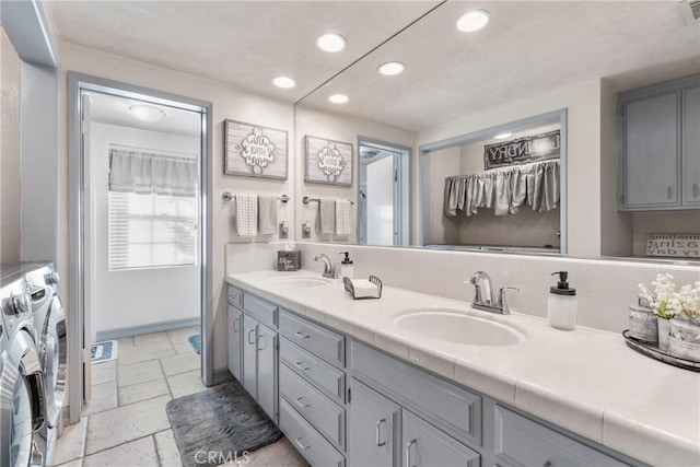 full bath with a sink, stone tile floors, recessed lighting, separate washer and dryer, and double vanity