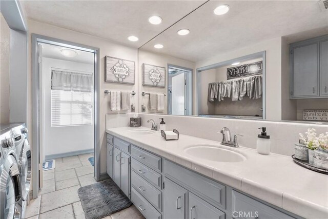 full bathroom with washing machine and clothes dryer, a sink, stone tile flooring, double vanity, and recessed lighting