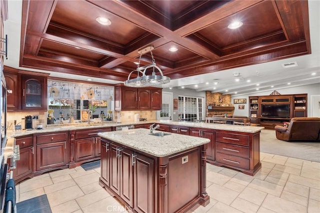 kitchen featuring a sink, a center island with sink, dark brown cabinets, open floor plan, and beamed ceiling