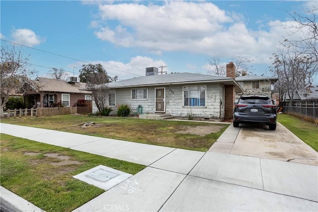 view of front facade with a front yard, fence, a chimney, concrete driveway, and central air condition unit