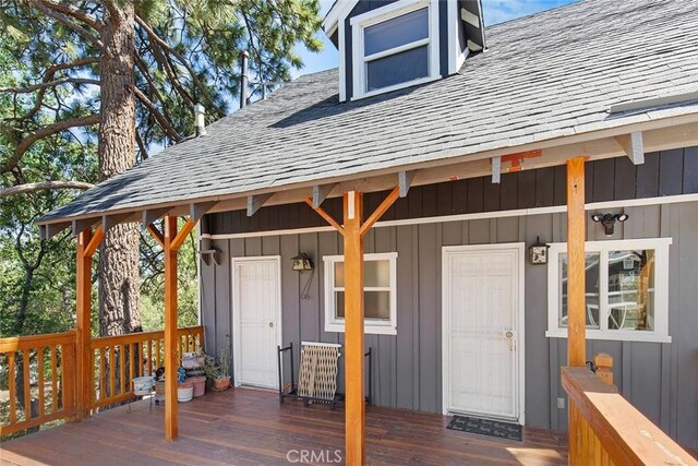 entrance to property with a wooden deck, board and batten siding, and a shingled roof