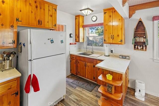 kitchen with wood finished floors, freestanding refrigerator, a sink, light countertops, and brown cabinets