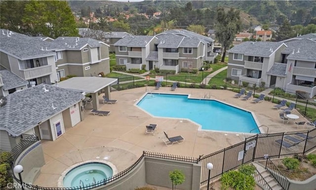 pool with a residential view, a hot tub, and fence