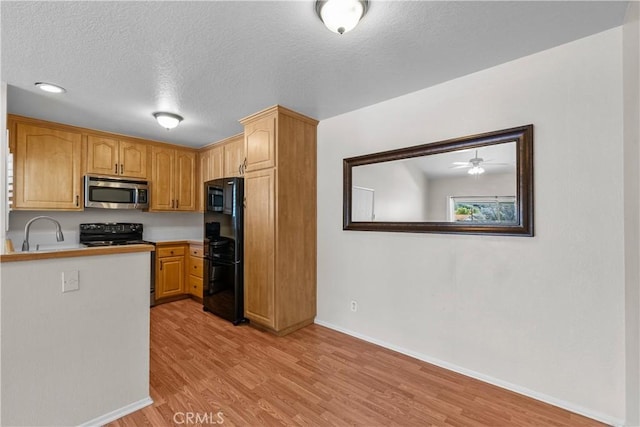 kitchen with light wood finished floors, stainless steel microwave, electric range oven, freestanding refrigerator, and a sink